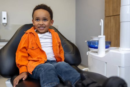 Téléchargez les photos : En dentisterie. Garçon à la peau foncée regardant heureux après la session du dentiste - en image libre de droit
