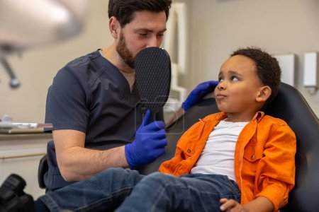 Téléchargez les photos : En dentisterie. Dentiste masculin travaillant avec un garçon à la peau foncée - en image libre de droit