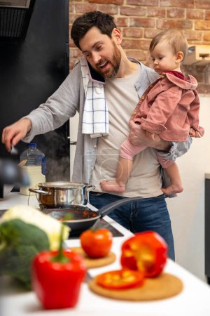 Foto de Multitarea padre cuidado de niños, cocinar el desayuno y hablar por teléfono inteligente en casa en kitchenn. - Imagen libre de derechos