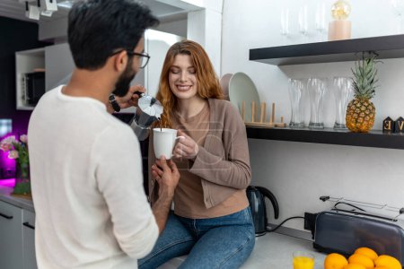 Téléchargez les photos : Délicieuse femme buvant du café avec l'homme assis sur le comptoir de la cuisine. - en image libre de droit