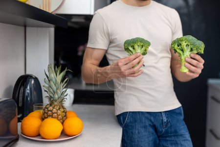 Téléchargez les photos : Homme inconnu tenant vert brocoli frais debout dans la cuisine moderne à la maison. - en image libre de droit