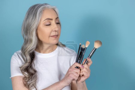 Téléchargez les photos : Maquillage. Belle femme âgée avec brosses pour le visage - en image libre de droit
