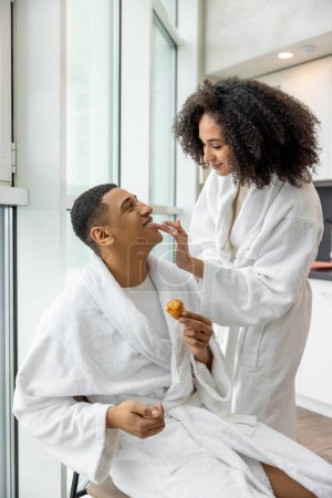 Photo for Breakfast. Young couple in white bath robes habing breakfast and looking happy - Royalty Free Image