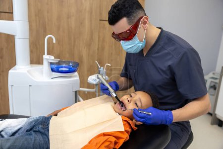 Téléchargez les photos : En dentisterie. Docteur en lunettes traitant les dents des garçons - en image libre de droit