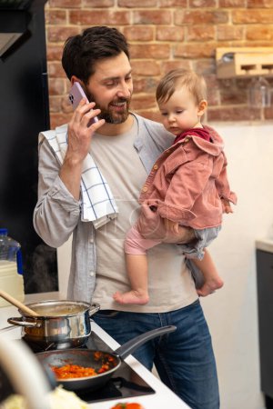 Foto de Padre ocupado cuidando de la niña haciendo comida y hablando por teléfono móvil, hombre multitarea en casa en kitchenn. - Imagen libre de derechos