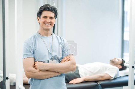 Téléchargez les photos : Docteur. Physiothérapeute masculin aux cheveux foncés regardant confiant et souriant - en image libre de droit