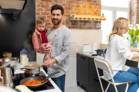 Téléchargez les photos : Famille heureuse à la maison dans la cuisine homme avec bébé cuisine faisant femme repas assis à la table. - en image libre de droit