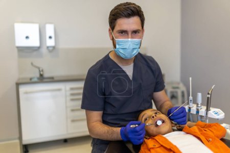 Foto de Odontología pediátrica. Odontólogo masculino con una máscara protectora que trabaja con poco paciente - Imagen libre de derechos