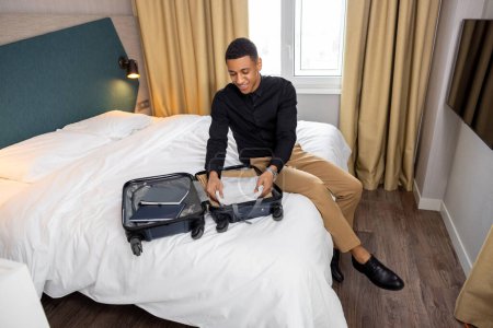 Téléchargez les photos : Déballer. Jeune homme déballer sa valise dans une chambre d'hôtel - en image libre de droit