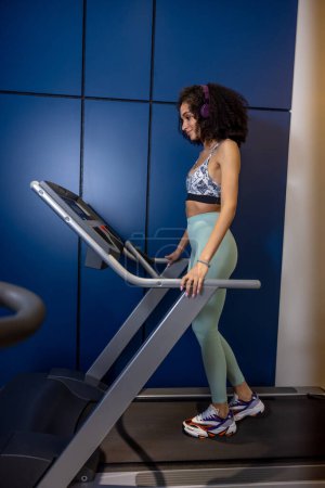Photo for On treadmill. Curly-haired young woman on a treadmill looking contented - Royalty Free Image