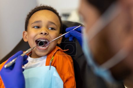 Foto de Cuidado de los dientes. Niño lindo de piel oscura que parece asustado mientras está sentado en la oficina de dentistas - Imagen libre de derechos