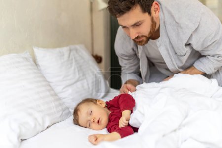 Photo for Father covering her sleeping baby with blanket at home. - Royalty Free Image