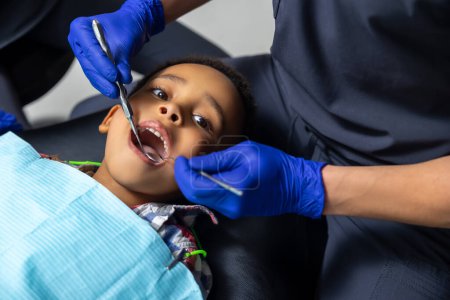 Téléchargez les photos : En dentisterie. Dentiste traitant les dents de garçons à la peau foncée - en image libre de droit