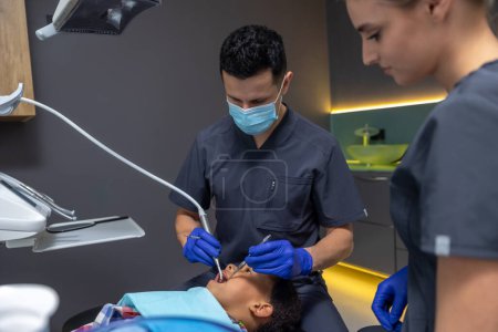Téléchargez les photos : En dentisterie. Homme médecin à la recherche concentré tout en traitant les dents des garçons - en image libre de droit