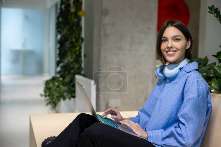 Téléchargez les photos : Souriant heureux attrayant jeune employée à distance travaillant sur l'ordinateur portable dans le centre d'affaires - en image libre de droit