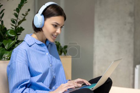 Photo for Smiling contented cute young Caucasian female in the wireless headphones working on the portable computer - Royalty Free Image
