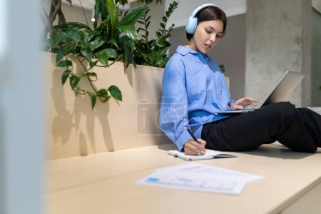 Foto de Mujer concentrada en los auriculares escuchando algo en el portátil y escribiendo en el portátil - Imagen libre de derechos
