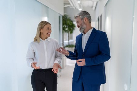 Téléchargez les photos : Agréable homme d'affaires élégant communiquant avec sa collègue féminine dans le couloir de bureau - en image libre de droit