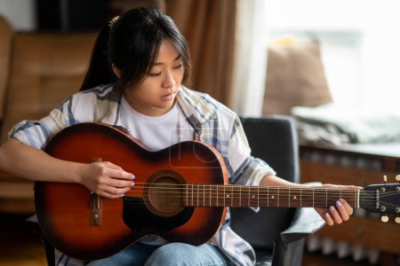 Foto de Tocando guitarra. Joven asiática chica jugando la guitarra en casa - Imagen libre de derechos
