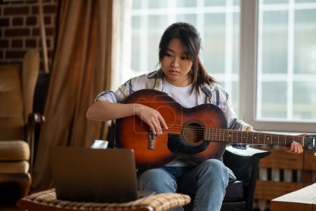 Téléchargez les photos : Cours de musique en ligne. Jeune fille asiatique ayant une classe en ligne sur jouer de la guitare - en image libre de droit