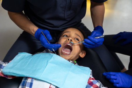 Téléchargez les photos : En dentisterie. Garçon à la peau foncée qui a peur des outils médicaux - en image libre de droit