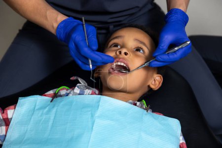 Téléchargez les photos : En dentisterie. Garçon à la peau foncée qui a peur des outils médicaux - en image libre de droit