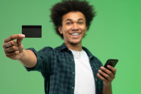 Téléchargez les photos : Africain américain jeune homme avec smartphone et carte de crédit dans les mains - en image libre de droit