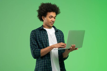 Téléchargez les photos : La technologie. Jeune homme américain africain en chemise à carreaux avec un ordinateur portable - en image libre de droit
