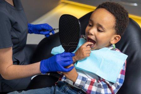 Téléchargez les photos : En dentisterie. Docteur donnant miroir au garçon à la peau foncée - en image libre de droit