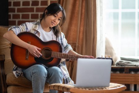 Foto de Tocando guitarra. Joven asiática chica jugando la guitarra en casa - Imagen libre de derechos