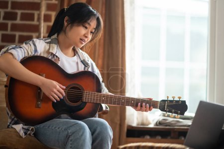 Photo for Online music class. Young asian girl having an online class on playing guitar - Royalty Free Image