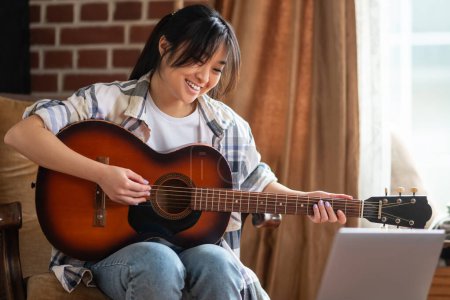 Photo for Playing guitar. Young asian girl playing the guitar at home - Royalty Free Image