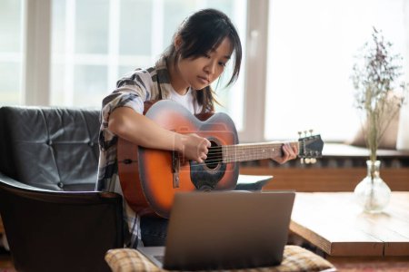 Foto de Clase de música en línea. Joven asiática chica tener un en línea clase en jugar guitarra - Imagen libre de derechos