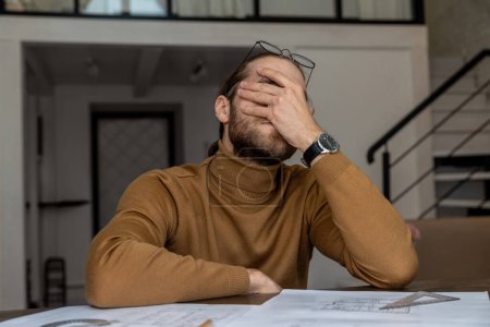 Photo for Exhausted tired young bearded young engineer architect working on new design of house, creating blueprint, being overworked. - Royalty Free Image