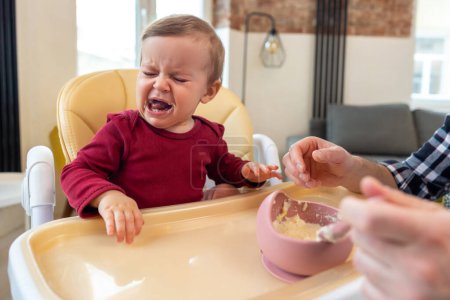 Téléchargez les photos : Enfant petite fille pleurant et ne veulent pas manger de la nourriture de son père qui se nourrit avec une cuillère. - en image libre de droit