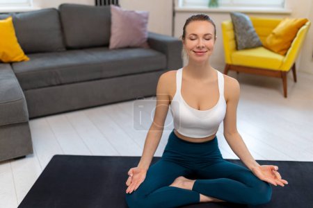 Téléchargez les photos : Femme sportive en vêtements de sport pratiquant le yoga et méditant sur tapis d'exercice à l'intérieur de la maison. - en image libre de droit
