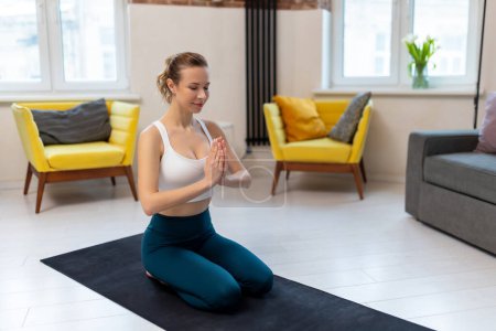 Foto de Mujer atlética en ropa deportiva practicando yoga y meditando en la esterilla de ejercicio en el interior del hogar. - Imagen libre de derechos