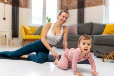 Photo for Young sporty mother in sportswear and baby girl working out exercising together at home in living room. - Royalty Free Image