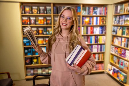 Photo for In library. Pretty blonde woman standing with books in library - Royalty Free Image