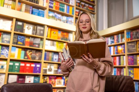 Téléchargez les photos : À la bibliothèque. Jolie femme blonde debout avec des livres à la bibliothèque - en image libre de droit