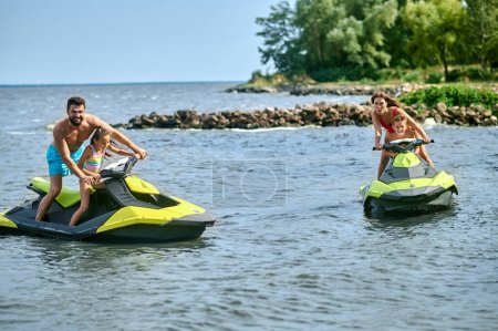 Vater, Mutter, Tochter und Sohn rasen auf Jetskis und genießen Wasserfahrzeuge im Meer, aktive Sommerzeit.