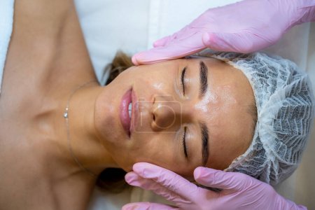 Téléchargez les photos : Massage du visage après la procédure de soins de la peau dans un salon de beauté, un cosmétologue, une clinique esthétique. - en image libre de droit