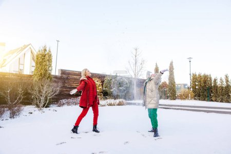 Photo for Smiling joyous blonde young woman and her cheerful female parent throwing snow in the air - Royalty Free Image