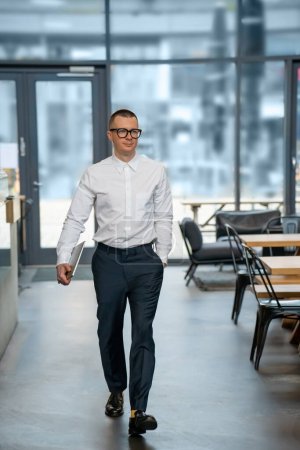 Téléchargez les photos : Homme d'affaires exécutif tenant un ordinateur portable fermé portant une chemise blanche marchant jusqu'au café pour faire une pause. - en image libre de droit