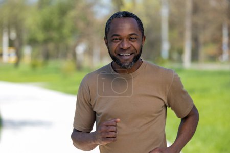 Téléchargez les photos : Du jogging. Homme mûr afro-américain jogging dans le parc et l'air satisfait - en image libre de droit