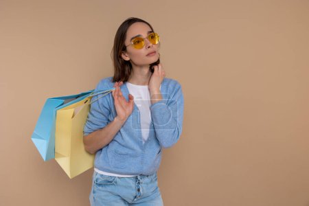 Foto de Mujer soñadora pensativa en ropa casual disfrutando de espacio de copia de compras aislado sobre fondo beige. - Imagen libre de derechos