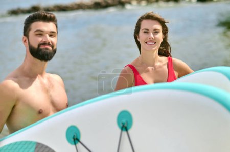 Foto de Atractivo hombre y mujer jóvenes surfistas en la playa, disfrutando de vacaciones cerca del mar y el deporte extremo, expresando emociones positivas. - Imagen libre de derechos