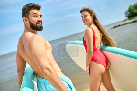 Photo for Couple with surfboards on beach, man and woman in swimsuits holding surfboards on sea coast at summertime. - Royalty Free Image
