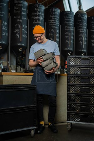 Foto de Camarero barista con sombrero y vasos descarga nuevo lote de café para la elaboración de café en la cafetería. - Imagen libre de derechos
