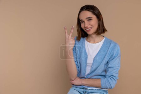 Foto de Mujer atractiva en ropa casual mostrando el número dos con los dedos aislados sobre fondo beige. - Imagen libre de derechos